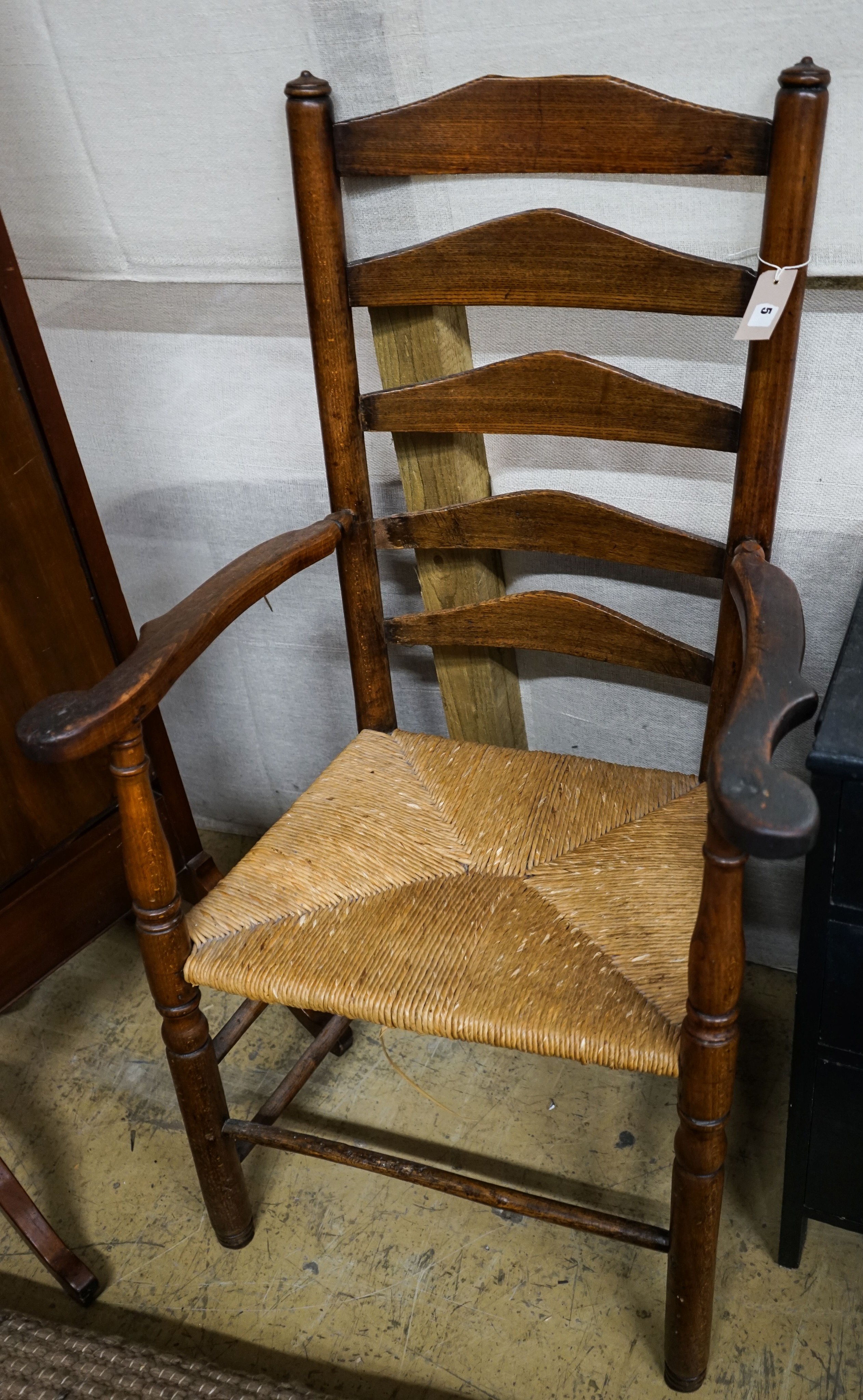 An early 19th century ash and elm rush seated ladder back elbow chair, width 63cm, depth 44cm, height 107cm